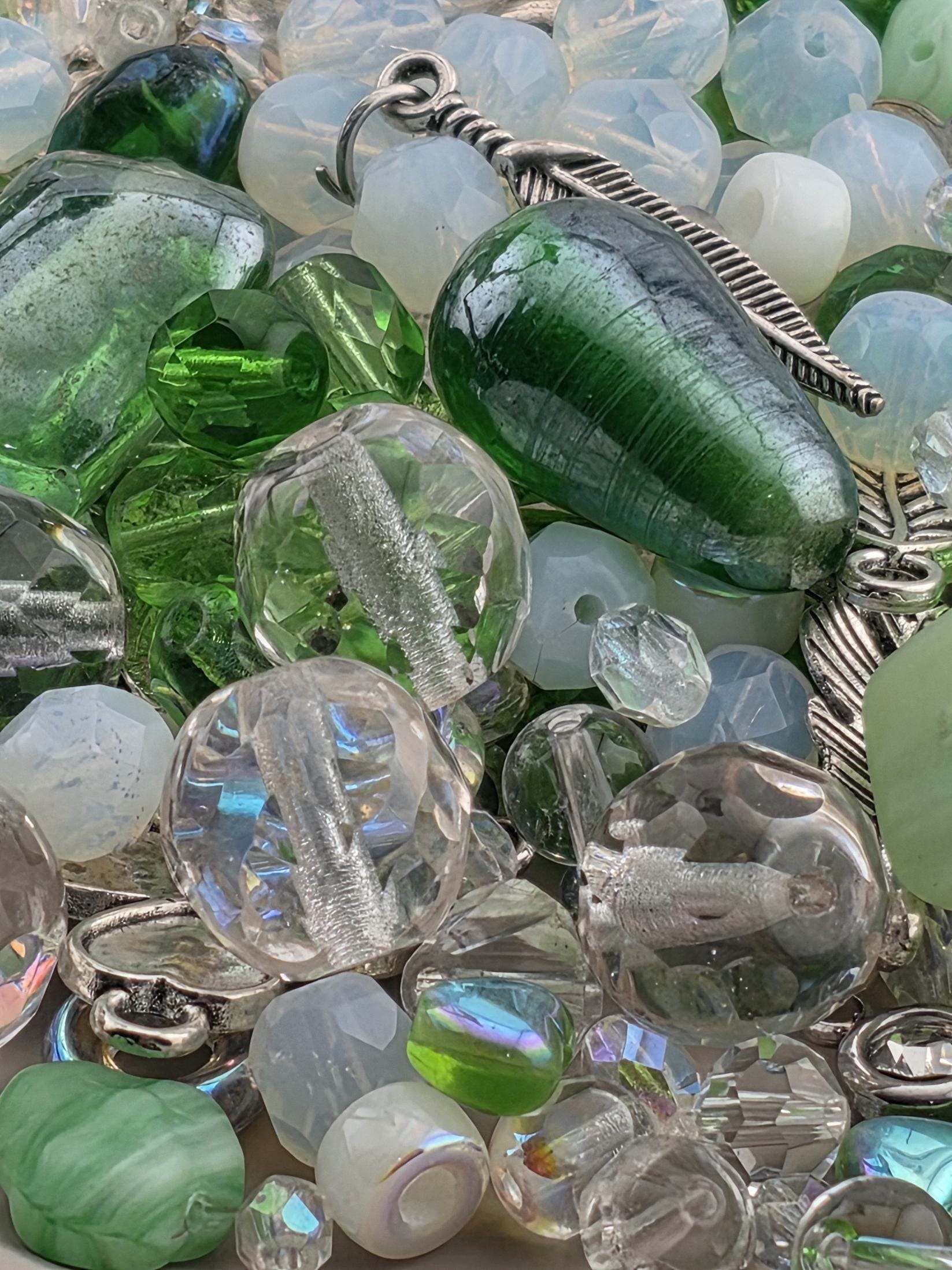 The image is a close-up of various glass beads and gemstones, including clear and green glass beads, as well as some metal and stone beads.