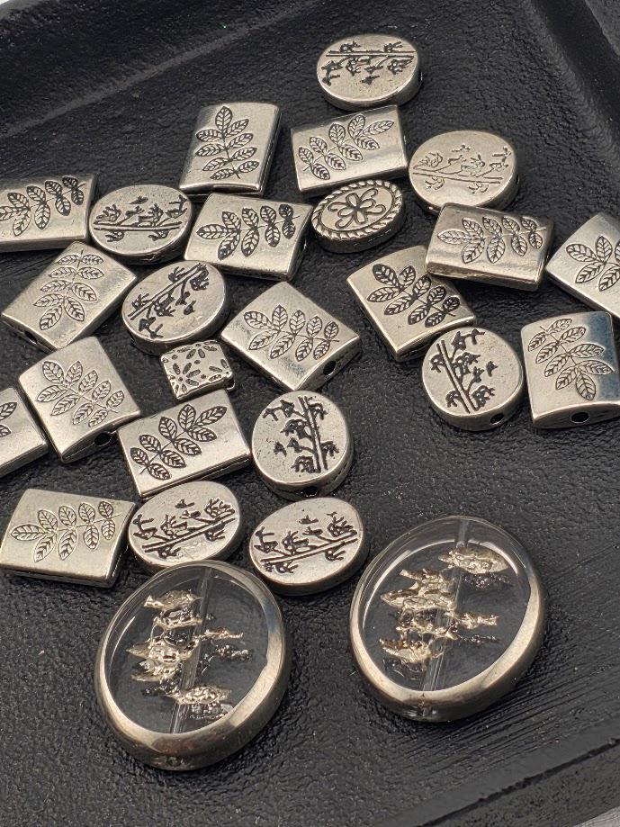 a collection of various metal beads and buttons with intricate leaf designs, arranged on a black surface.