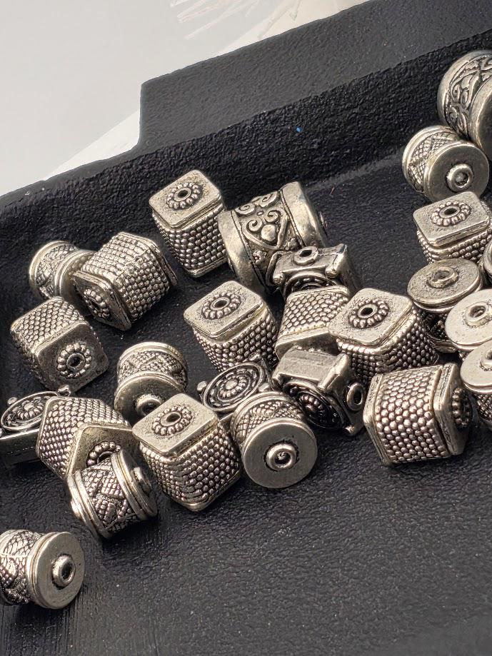 a collection of various metal beads, including square and round shapes, scattered on a black surface.