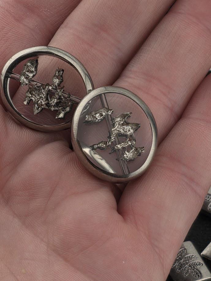 A close-up image of a person's hand holding two silver-colored metal objects, which appear to be small, circular or oval-shaped, with a reflective surface.