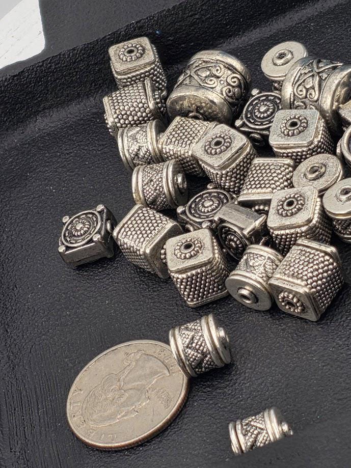 a collection of various metal beads and charms, including some that appear to be beads and charms, scattered on a black surface. There is also a coin visible in the foreground.
