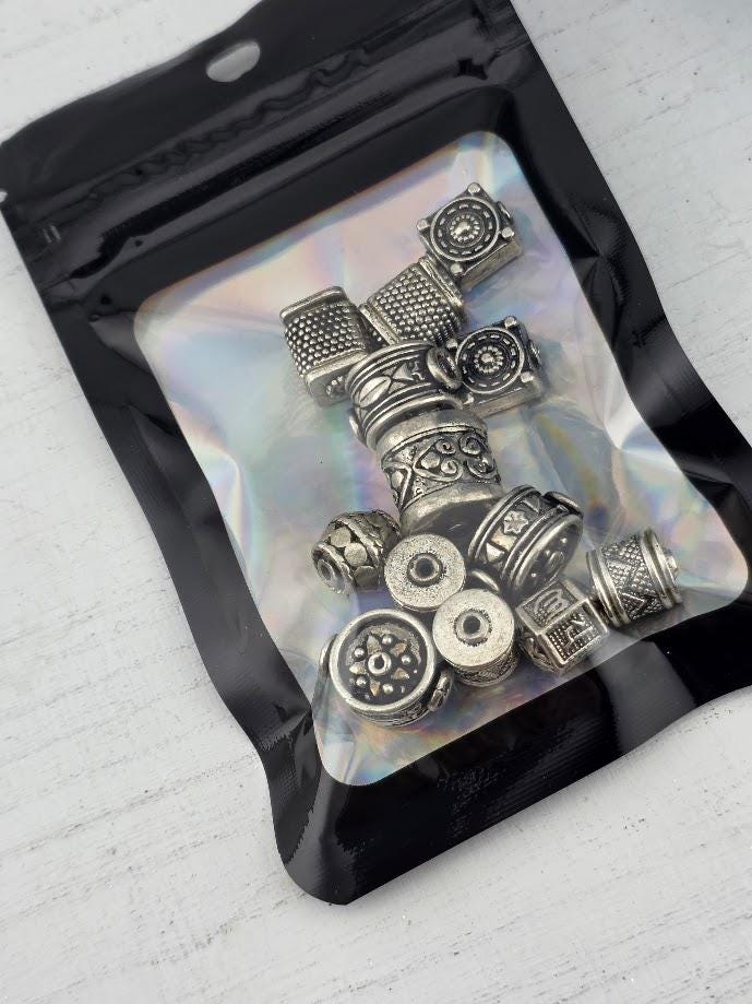 A clear plastic bag containing various metal beads and charms, including circular and rectangular shapes, arranged in a visually appealing manner.