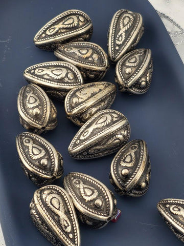 a collection of ornate metal beads or coins with intricate designs, arranged on a dark surface.