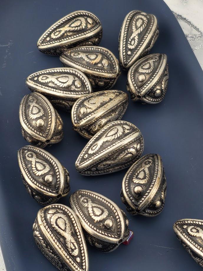 a collection of ornate metal beads or coins with intricate designs, arranged on a dark surface.