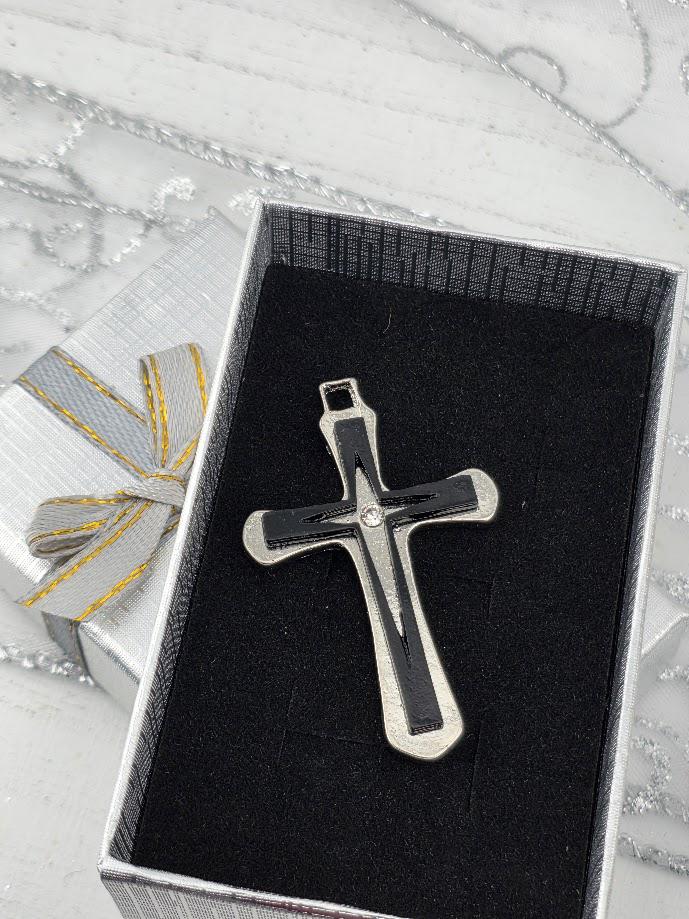 A silver cross pendant is displayed in a black box with a gold ribbon bow.