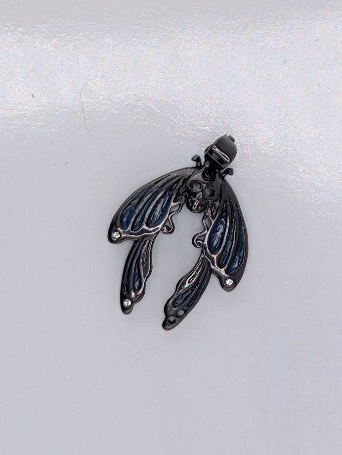 A black metal butterfly pendant with intricate details and a small head.