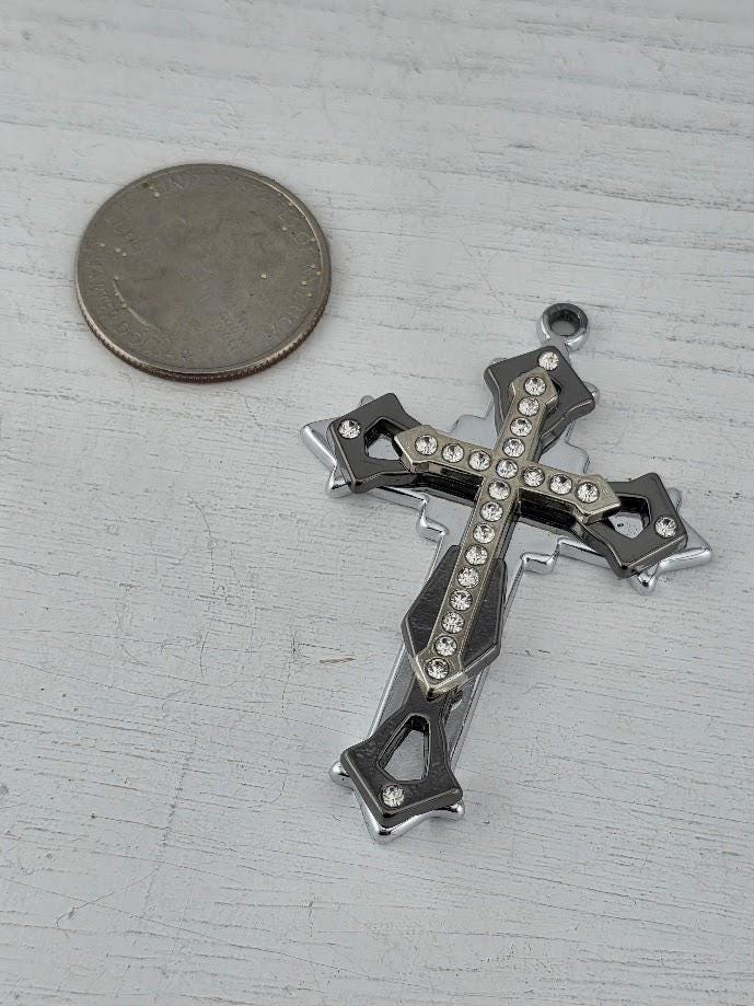 A silver cross pendant with rhinestones is displayed in a silver box with a gold ribbon bow.