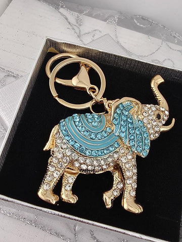 A decorative keychain in the shape of an elephant, with blue and gold accents, is displayed in a black box.