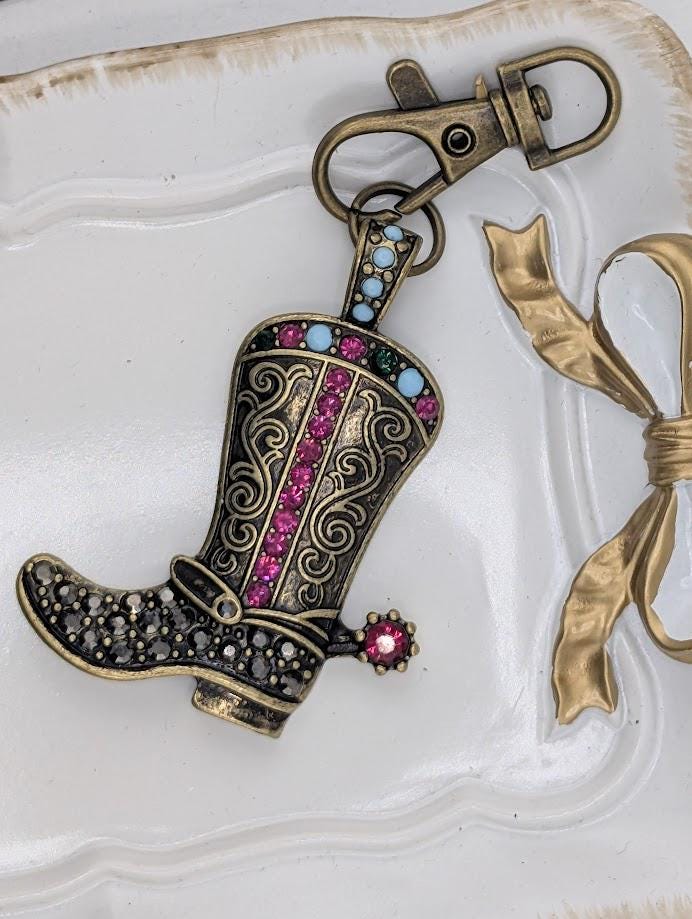 A decorative keychain in the shape of a cowboy boot, adorned with colorful gemstones and a bow.