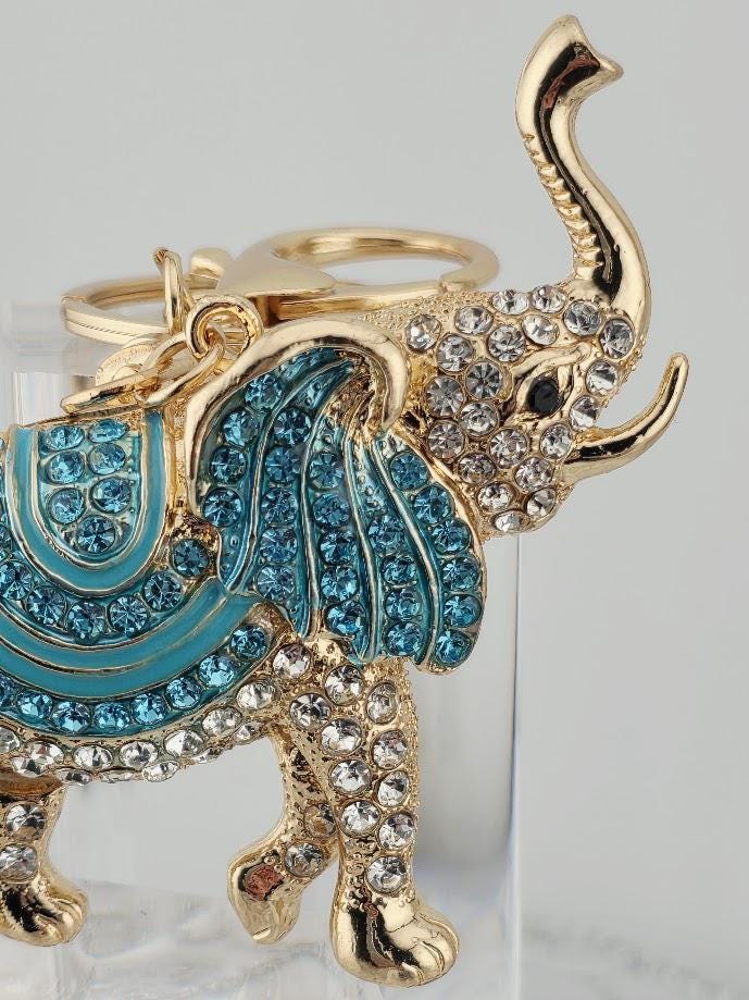 A decorative keychain in the shape of an elephant, with blue and gold accents, is displayed in a black box.