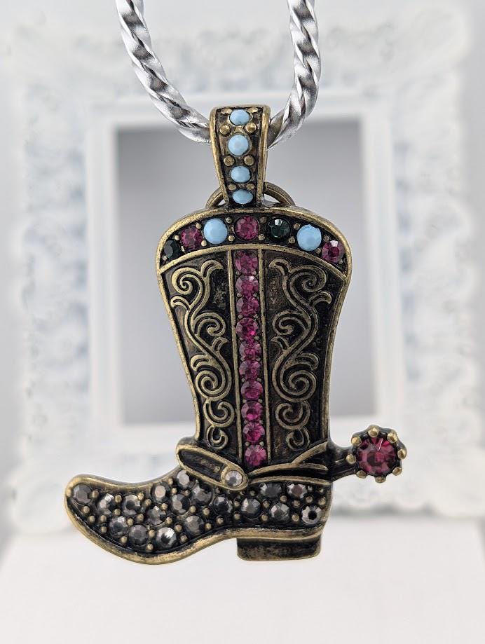A decorative pendant in the shape of a cowboy boot, adorned with colorful gemstones and a metallic chain.