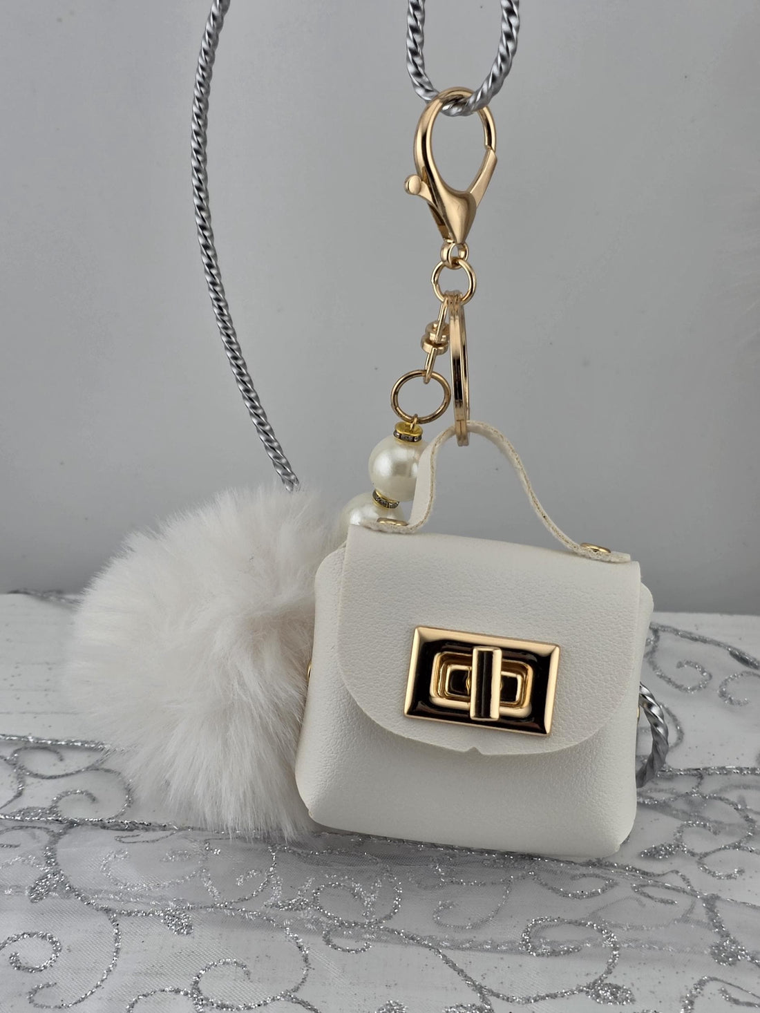 A white leather handbag with a gold lock and keychain attached to it.