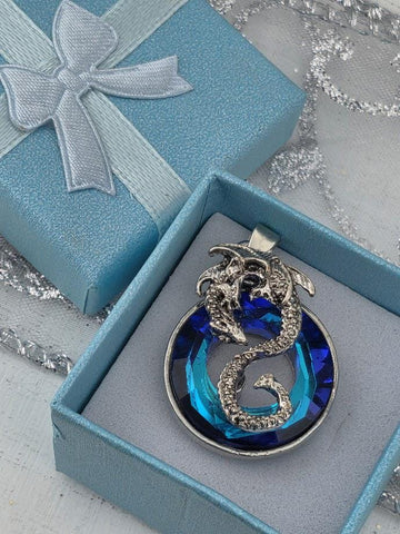 A blue gift box with a silver pendant featuring a blue gemstone and a silver dragon design, placed on a white surface.
