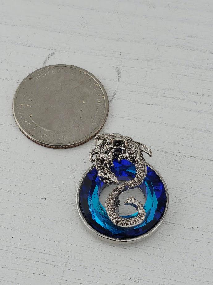 A silver-colored coin next to a blue gemstone pendant with a snake design.