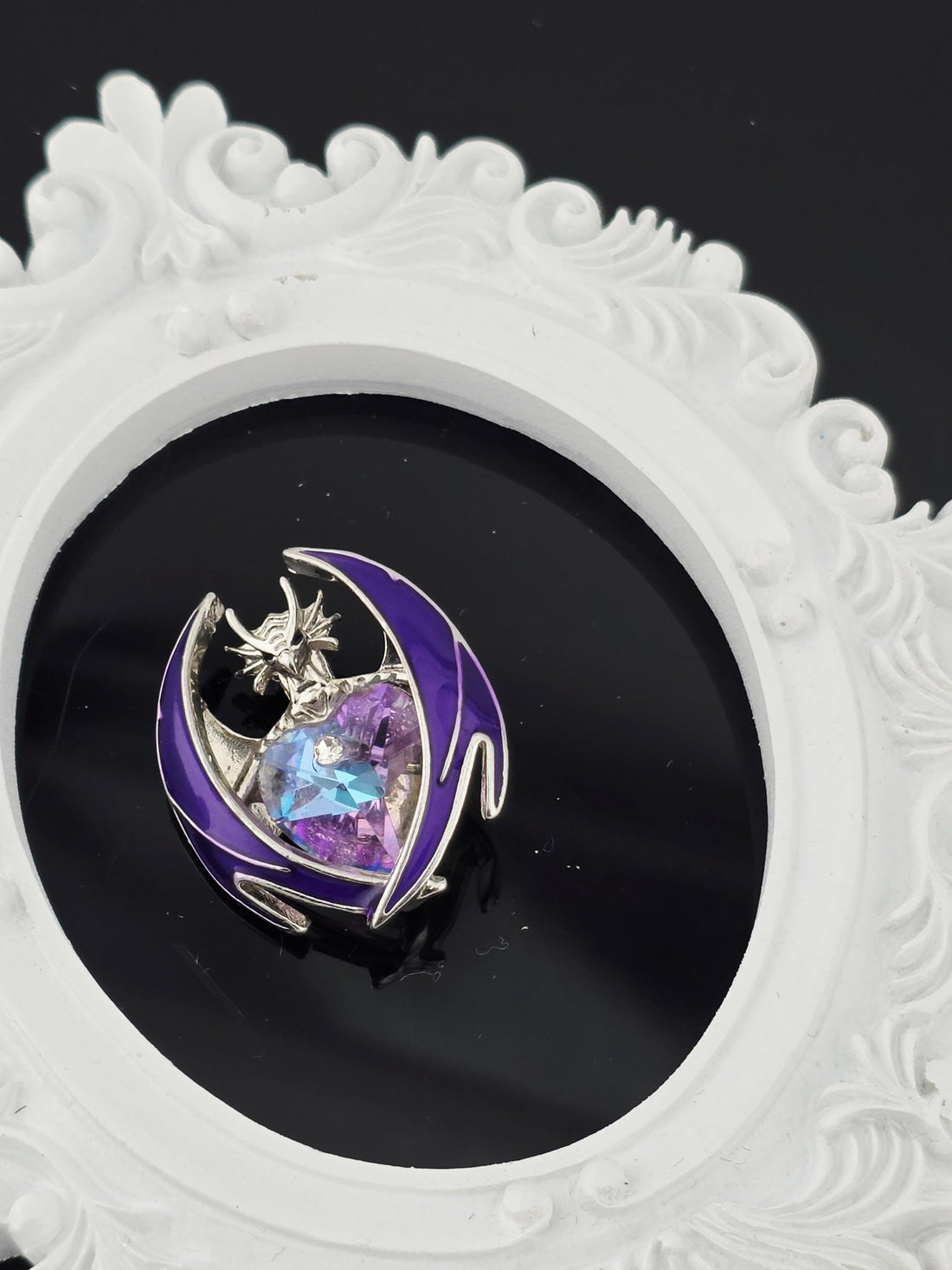 A purple brooch with a crescent moon design is displayed in a blue gift box with a white ribbon.