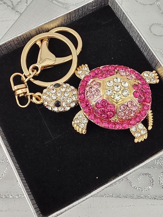 A keychain with a pink and gold turtle design, adorned with rhinestones and a gold-colored clasp.