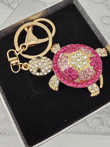 A keychain with a pink and gold turtle design, adorned with rhinestones and a gold-colored clasp.