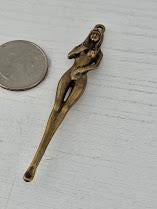 A small bronze sculpture of a woman is placed next to a coin on a white surface.