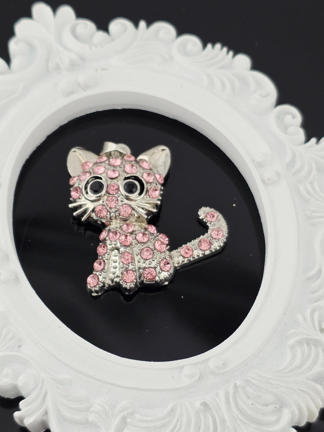 A decorative brooch in the shape of a cat, adorned with pink gemstones, is displayed in a blue gift box with a white ribbon bow.