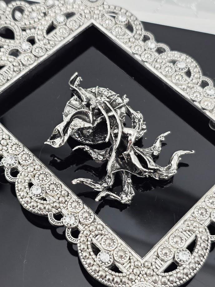 a silver-colored metal sculpture or ornament with a decorative frame, placed on a black surface.