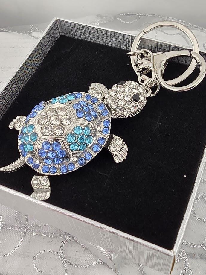 A silver keychain with a blue and white turtle design, adorned with rhinestones or crystals.