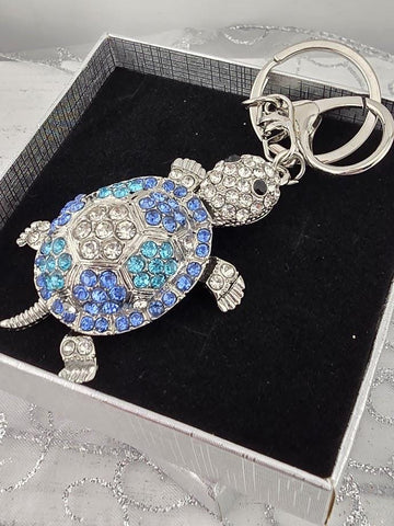 A silver keychain with a blue and white turtle design, adorned with rhinestones or crystals.
