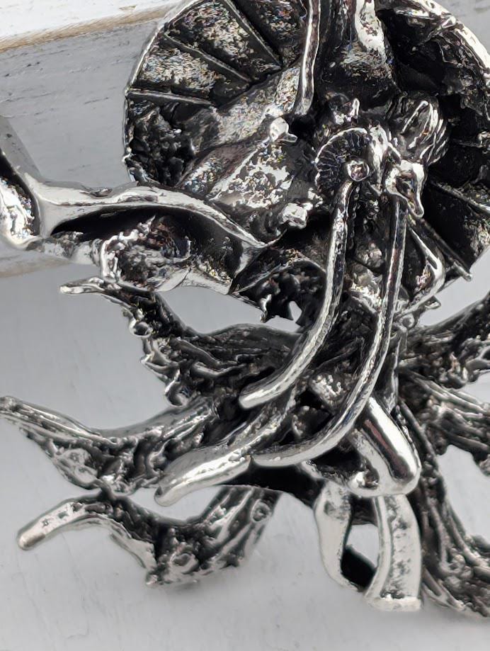 a silver-colored metal sculpture or ornament with a decorative frame, placed on a black surface.