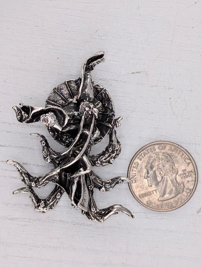 a silver-colored metal sculpture of an octopus or squid, with its tentacles spread out, placed next to a United States quarter coin.