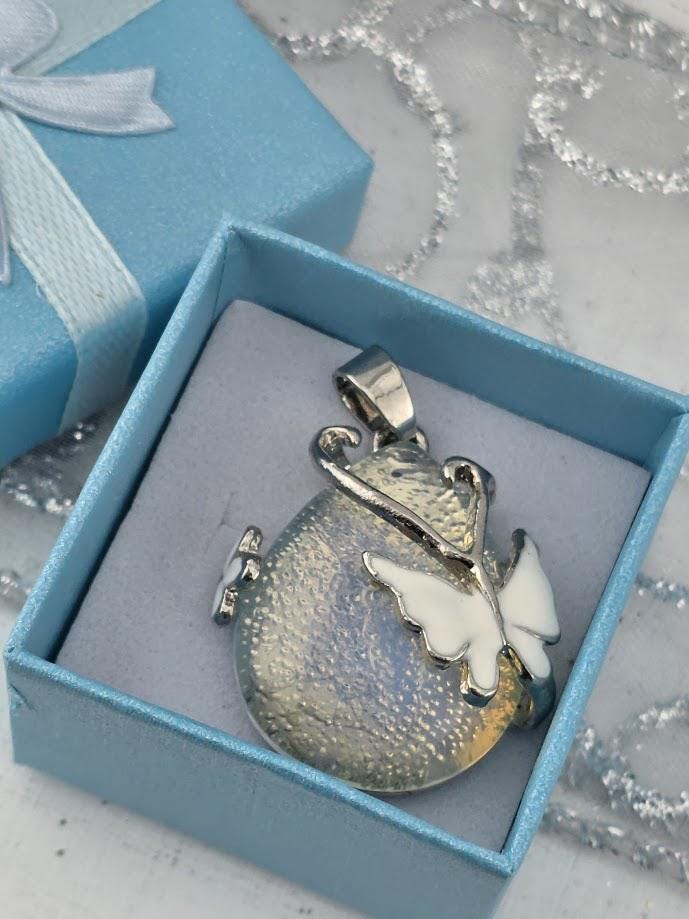 A silver pendant with a butterfly design is displayed in a blue gift box.
