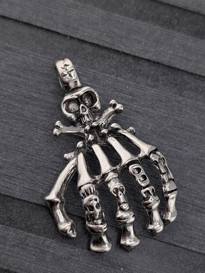 A silver-colored pendant in the shape of a hand with bones protruding from it, resting on a dark surface.