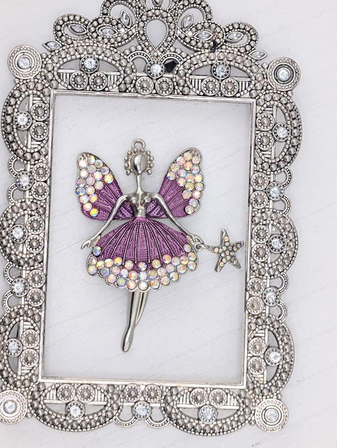 A silver-colored pendant in the shape of a fairy with wings and a star, set within an ornate, decorative metal frame.