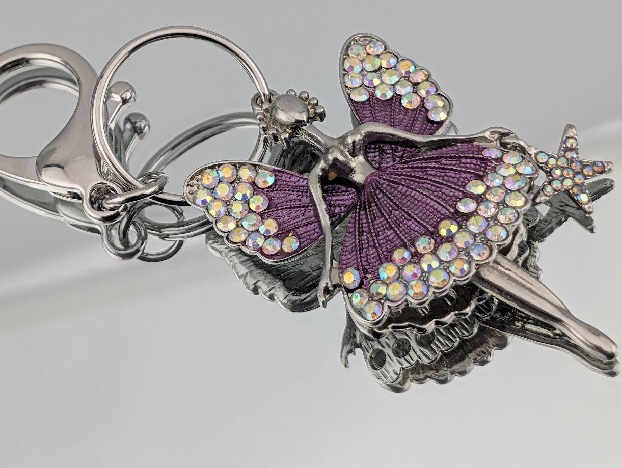 A keychain with a purple fairy design, featuring a star and a butterfly motif, adorned with rhinestones or crystals.