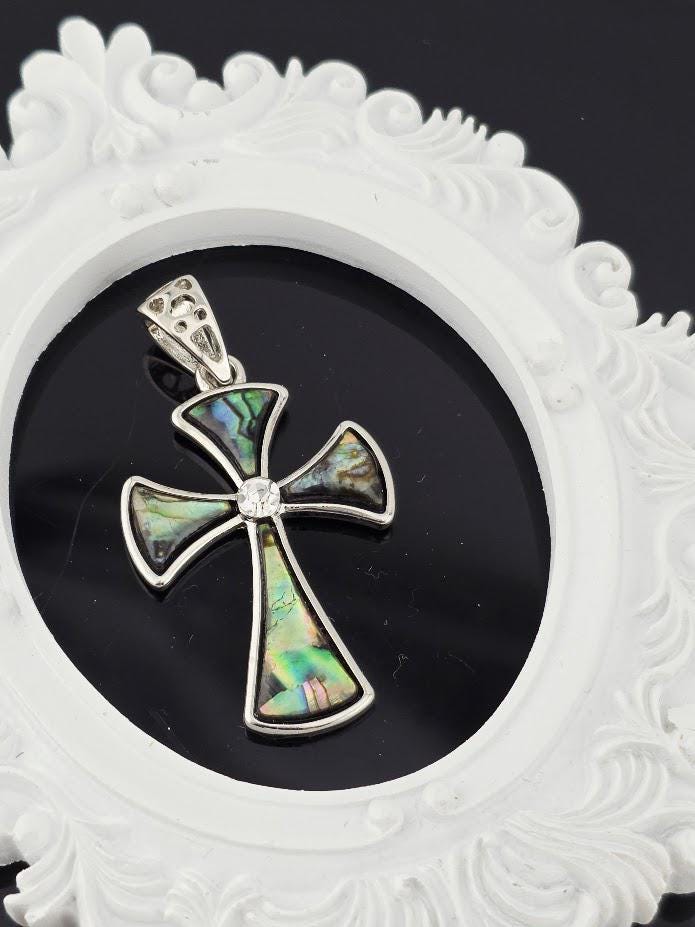 A silver cross pendant with colorful inlays is displayed in a white ornate frame against a dark background.