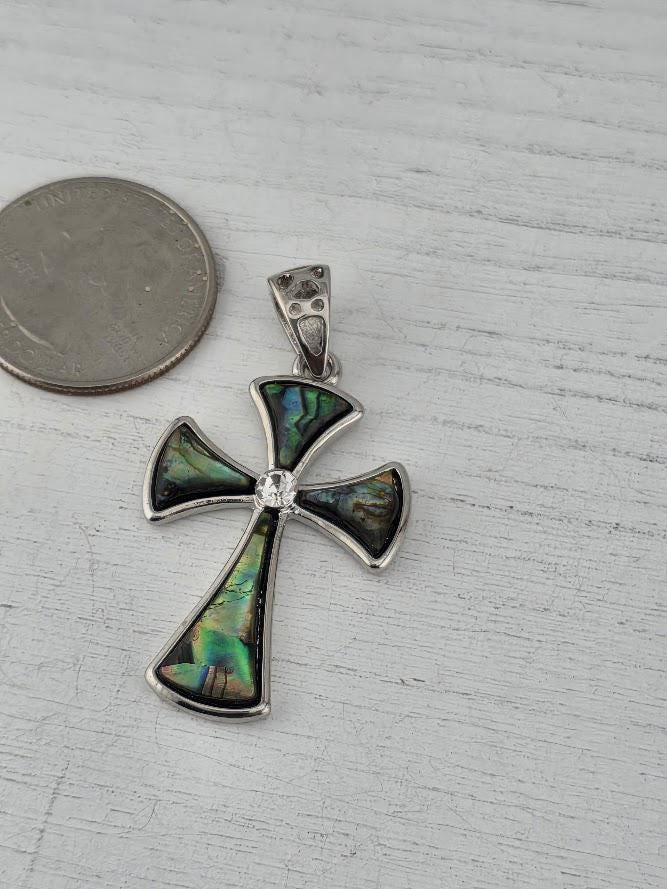 A silver-toned pendant cross with a gemstone in the center, placed next to a US quarter on a wooden surface.