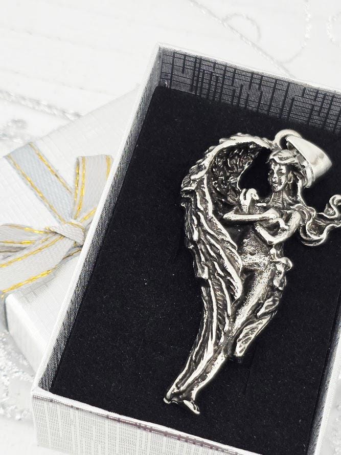 A silver pendant in the shape of a winged woman is displayed in a white box with a black interior.