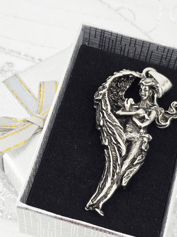 A silver pendant in the shape of a winged woman is displayed in a white box with a black interior.