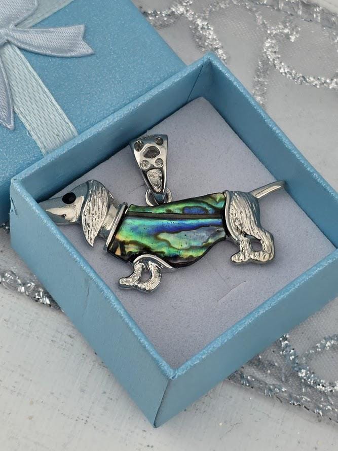 A pendant in the shape of a dog, made of a shiny material, is displayed in a blue jewelry box.