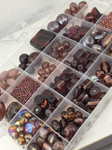 A clear plastic container filled with various beads and beads in different shapes and sizes, organized in rows and columns.