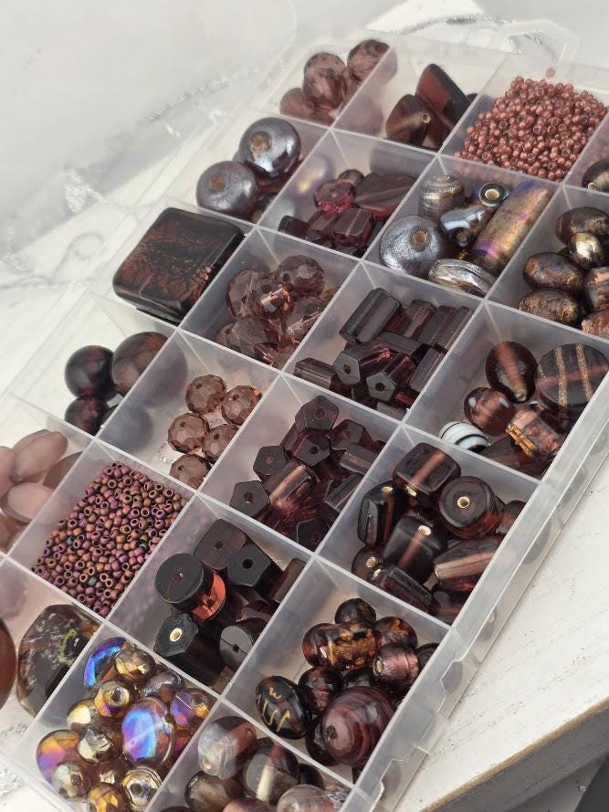 A clear plastic container filled with various beads and beads in different shapes and sizes, organized in rows and columns.
