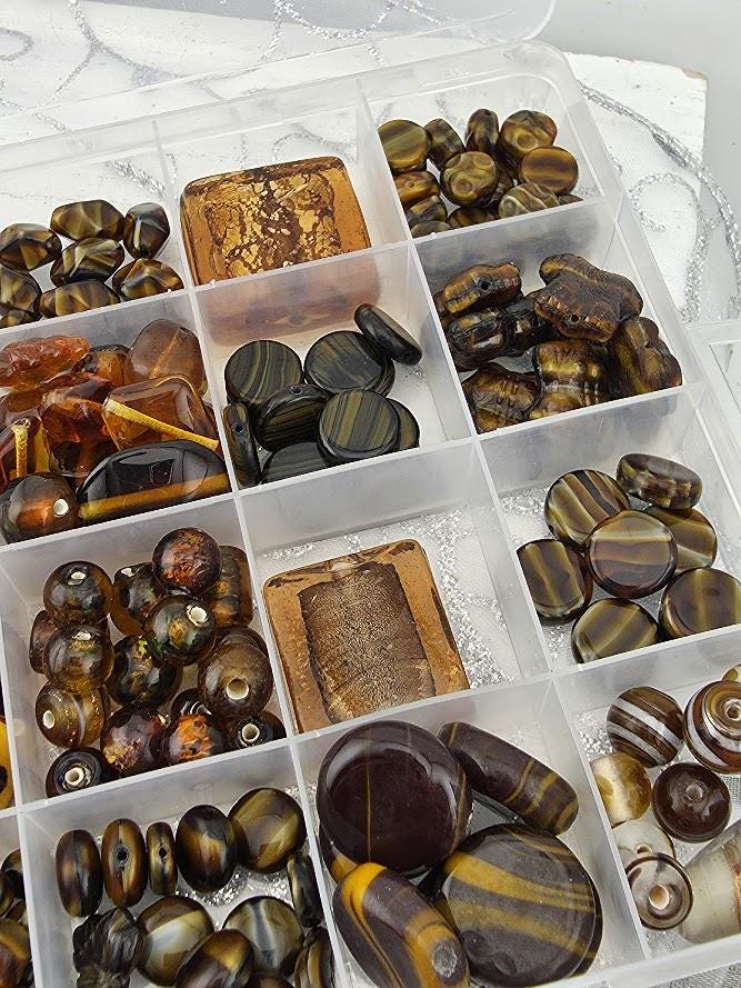 A clear plastic container filled with various beads and stones in different shapes, sizes, and colors.