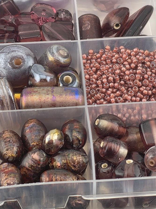 A collection of various beads and glass objects, including glass beads, metal beads, and glass beads, arranged in a transparent container.