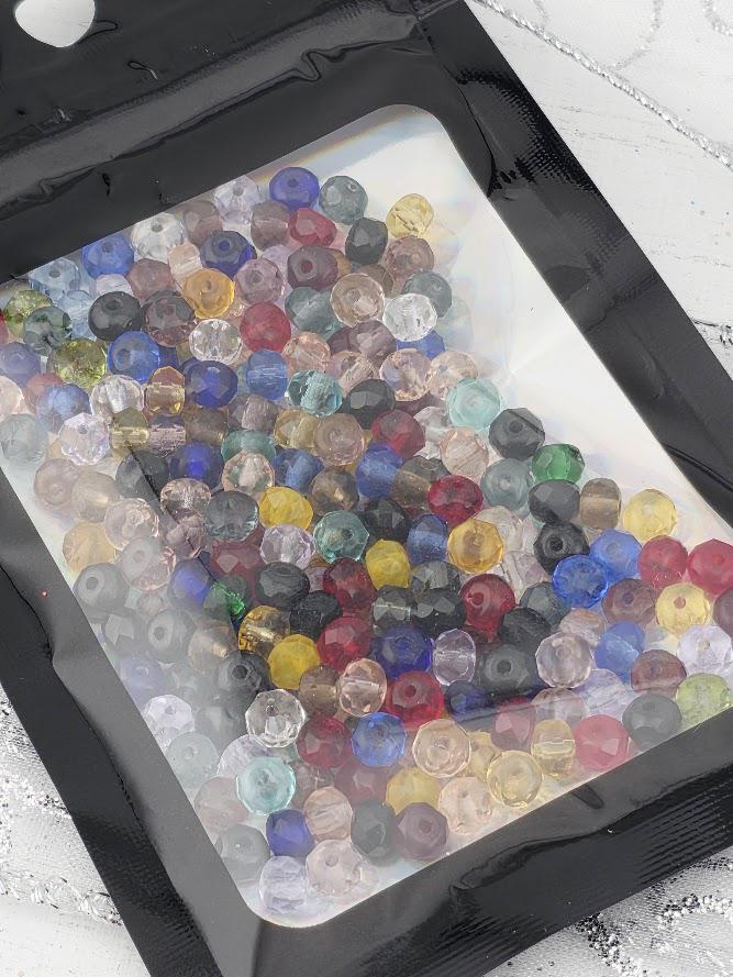 A clear plastic bag filled with a variety of colorful glass beads, including clear, blue, green, red, yellow, and multicolored glass beads.