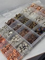 A clear plastic container filled with various beads, nuts, and coins, organized into multiple compartments.