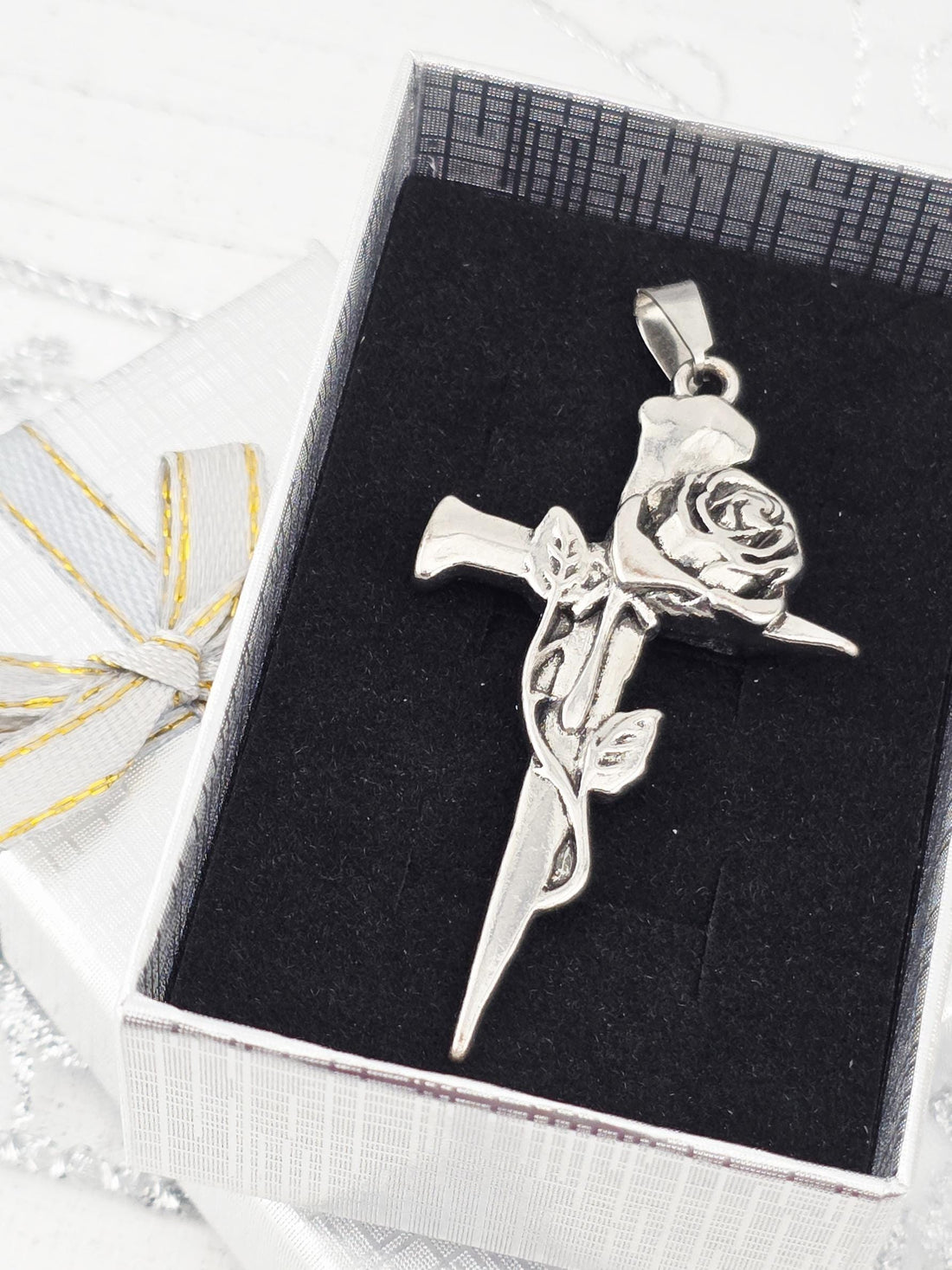 A silver-colored pendant in the shape of a rose is displayed in a black box with a white ribbon.