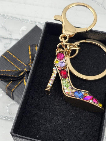 A keychain with a gold-colored shoe charm, adorned with colorful gemstones, is displayed in a black box.