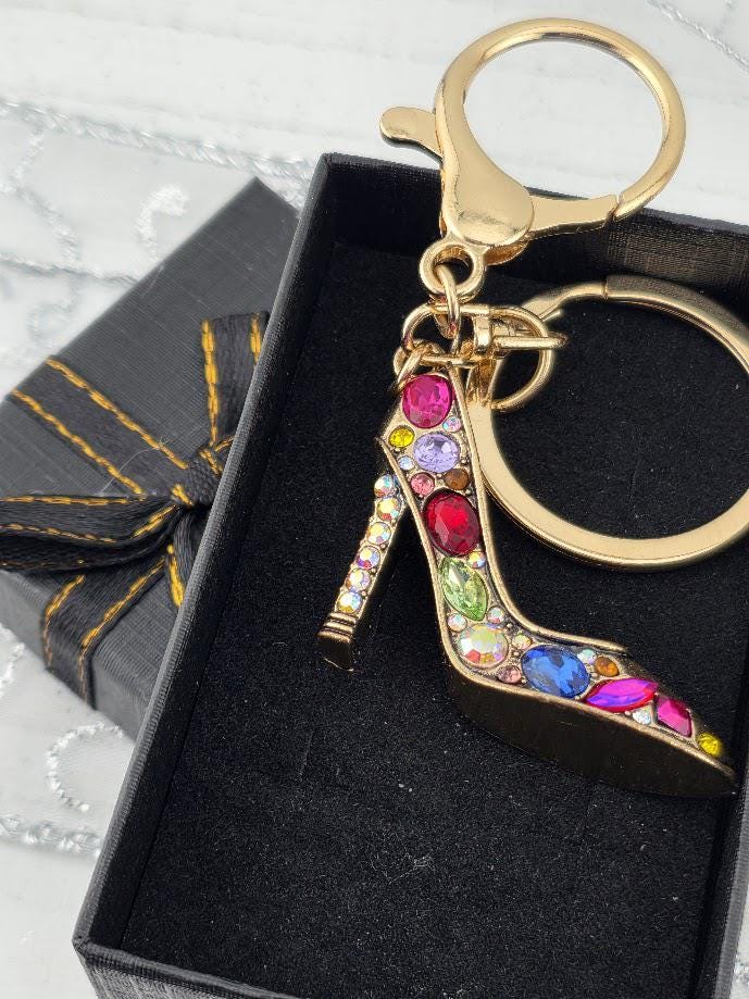 A keychain with a gold-colored shoe charm, adorned with colorful gemstones, is displayed in a black box.