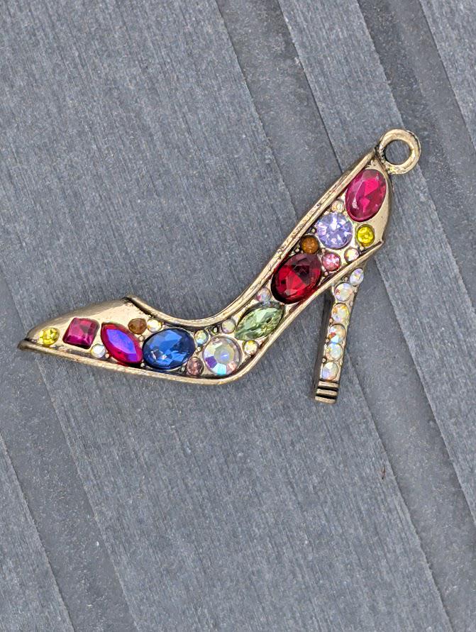 A decorative charm in the shape of a high-heeled shoe, adorned with various colorful gemstones.