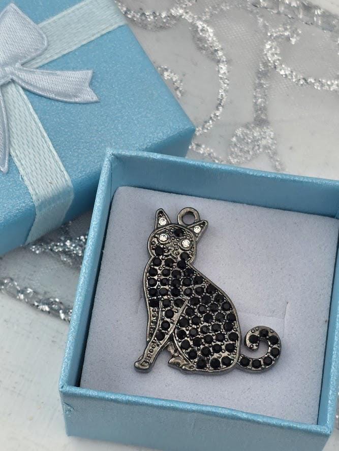 A blue gift box containing a silver cat charm with black gemstones.