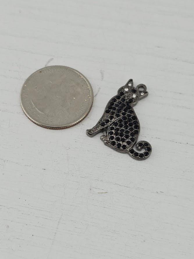 A silver coin next to a small metal cat charm on a white surface.