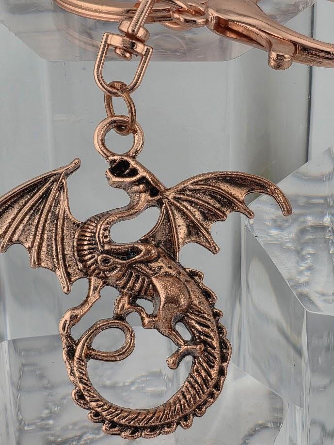 A copper-colored dragon keychain is displayed in a black box with a yellow ribbon bow.